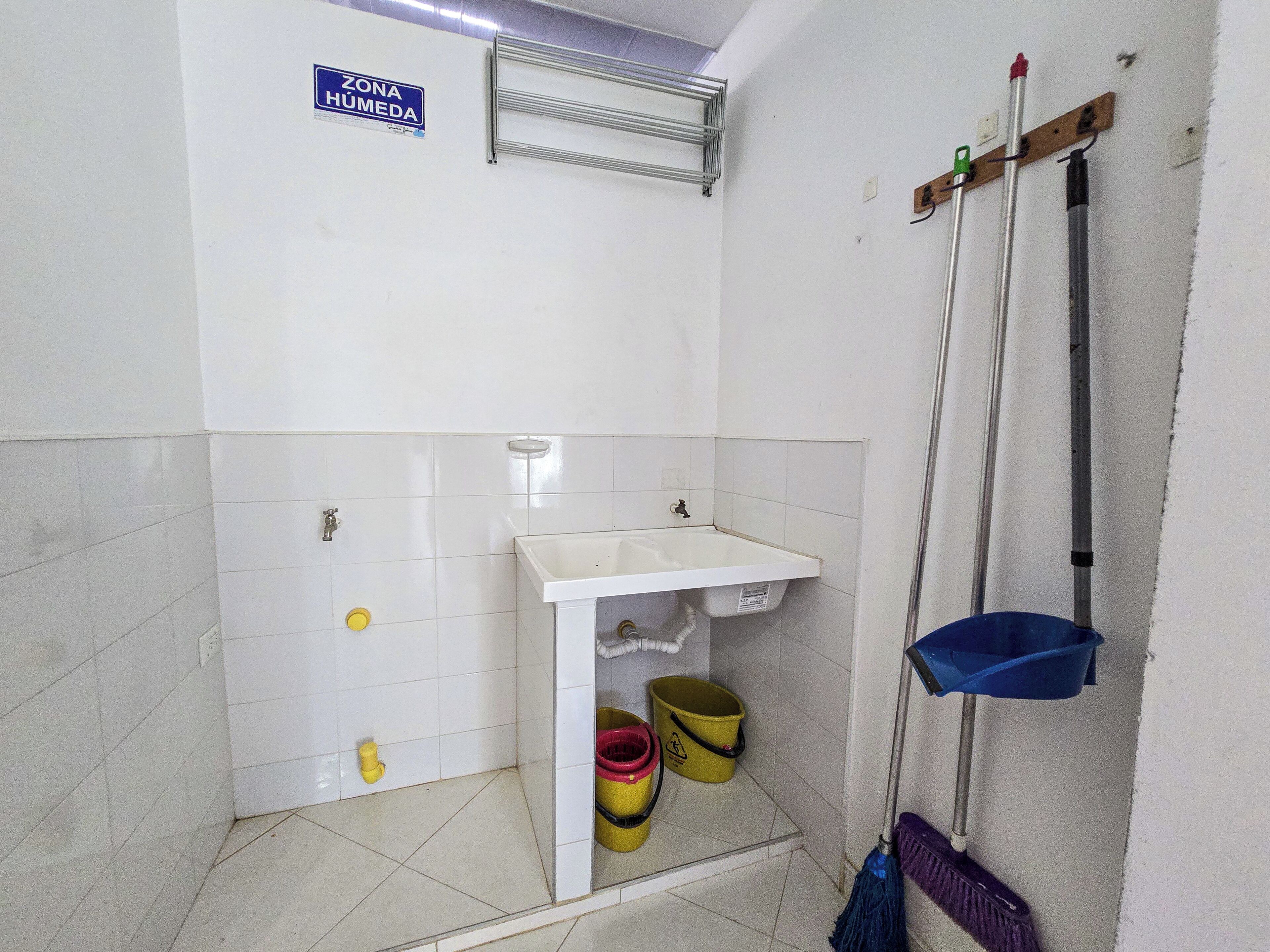 A bathroom with a sink, two yellow buckets, a mop, and a 'ZONA HÚMEDA' sign.