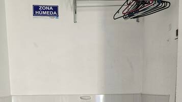 Un baño con un lavabo, un cubo amarillo, un trapeador y un letrero que dice 'ZONA HUMEDA'.