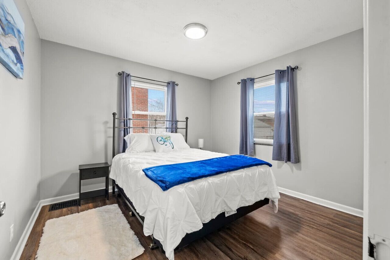 A bedroom with a bed, a nightstand, a window with curtains, and a white wall.