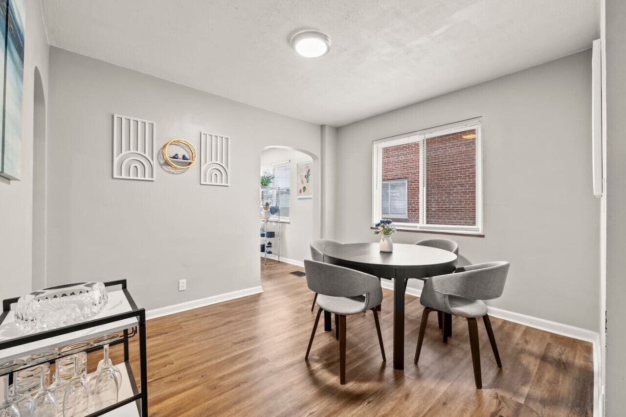 A dining area with a round table and four chairs, a small side table with glasses, and a wall with decorative panels.
