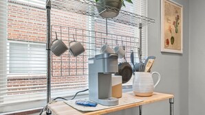 Una zona de cocina con cafetera, ollas colgadas y un cuadro de pared con temática de cactus.