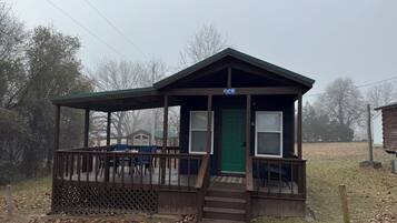 A small cabin with a porch, a green door, and a sign above the door.