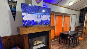 Un salon avec un téléviseur à écran plat fixé sur une cheminée en bois, une table à manger avec des chaises et un tapis décoré sur le thème du basketball.