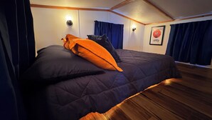 Une chambre à coucher avec un lit de couleur sombre, des poutres en bois au plafond et un tableau encadré au mur.