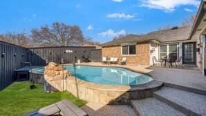 Un jardin avec une piscine, un espace barbecue et une terrasse aménagée avec du mobilier d’extérieur.