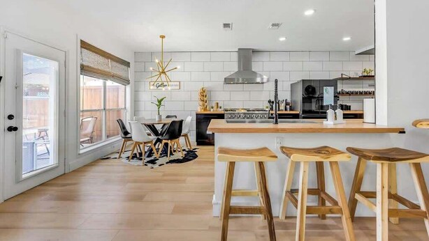 A modern kitchen with a central island, bar stools, and a dining area with chairs and a table.