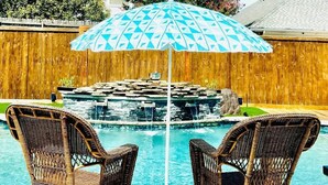 Two wicker rocking chairs by a pool with a blue umbrella.