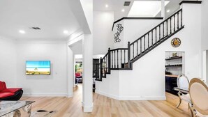 A spacious living area with a wooden floor, a red sofa, a glass coffee table, and a staircase with black railings.