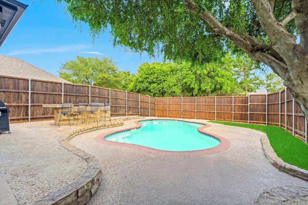 A backyard with a swimming pool, a barbecue area, and a wooden fence.
