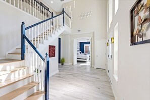 A spacious hallway with a wooden staircase and a bed visible in the background. - Luxe Modern Spacious Pool PingPong EV Sleeps 20! (Frisco)
