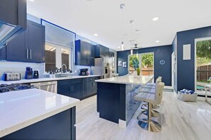 A modern kitchen with dark cabinets, a central island, and a bar area. - Luxe Modern Spacious Pool PingPong EV Sleeps 20! (Frisco)