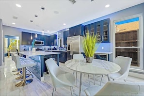 A modern kitchen with dark blue cabinets, stainless steel appliances, and a central island with seating. - Luxe Modern Spacious Pool PingPong EV Sleeps 20! (Frisco)