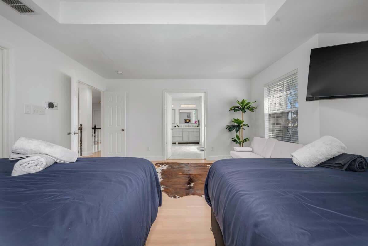Habitación de hotel con dos camas, piso de madera, televisor montado en la pared y una planta.