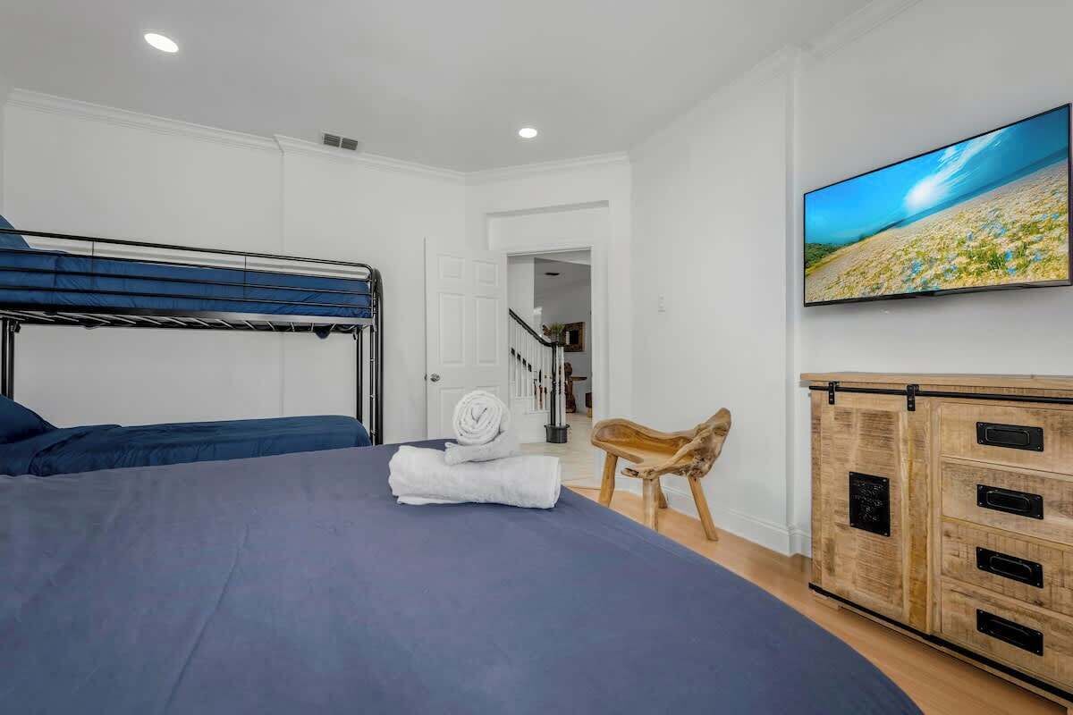 A bedroom with a bunk bed, a wooden cabinet, and a large TV displaying a beach scene.