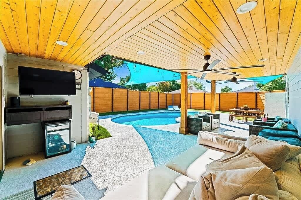 Un espacio exterior con piscina, techo de madera, ventiladores de techo y una zona de estar con cojines.