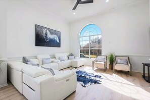 Ein geräumiges Wohnzimmer mit einem weißen Modulsessel, einem großen Fenster und einem aufgehängten Bild eines Pferdes.