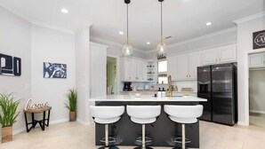 A modern kitchen with white cabinets, a central island with bar stools, and a stainless steel refrigerator. - Exquisite 6 BR Retreat PoolSpa 4.5 Bath Sleeps 20+ (Richardson)