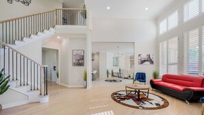 A spacious living area with a staircase, a red sofa, a coffee table, and a cowhide rug. - Exquisite 6 BR Retreat PoolSpa 4.5 Bath Sleeps 20+ (Richardson)