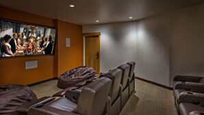 Una habitación con una pantalla grande mostrando una escena de película, sofás reclinables y piso alfombrado.