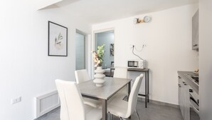 A modern kitchen with white cabinetry, a dining table with chairs, and a vase with flowers. - Costa Ovest Apartments (Nurachi)