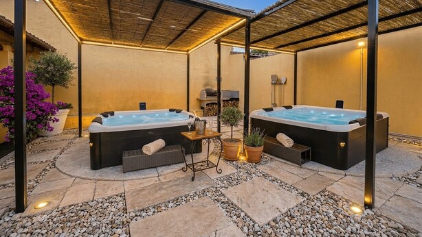 A covered outdoor area with two hot tubs, a small table with a drink, and potted plants. - Costa Ovest Apartments (Nurachi)