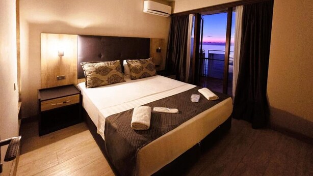 Una habitación de hotel con una cama grande, una mesita de noche, un equipo de aire acondicionado y vistas a la puesta de sol desde la ventana.
