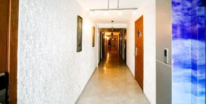 Un pasillo de hotel con paredes de ladrillo blanco, puertas de madera y suelo de color claro.