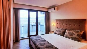 Habitación de hotel con una cama grande, cabecera, ventana con cortinas y vista al mar.