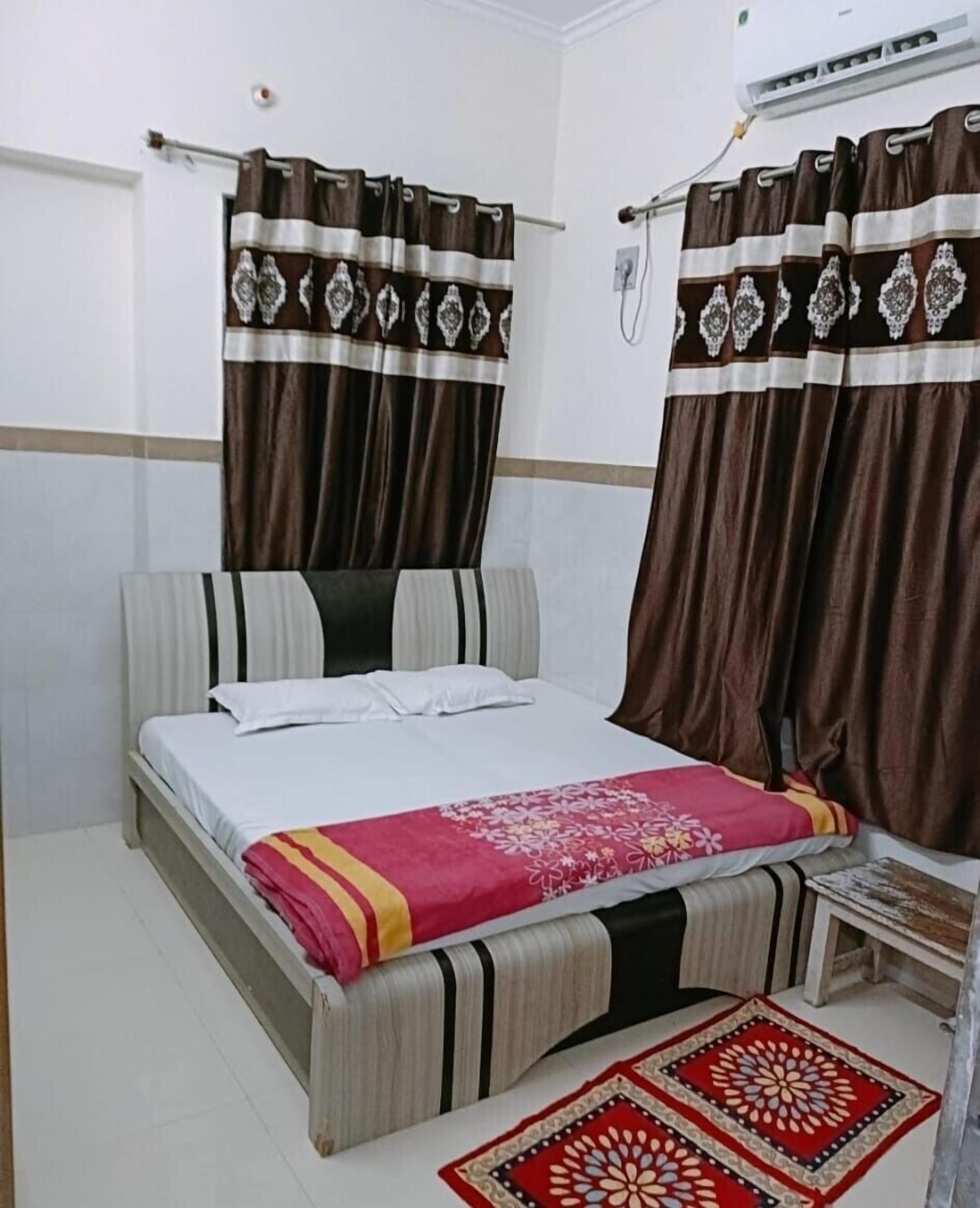 A bedroom with a bed, curtains, a small table, and a rug.