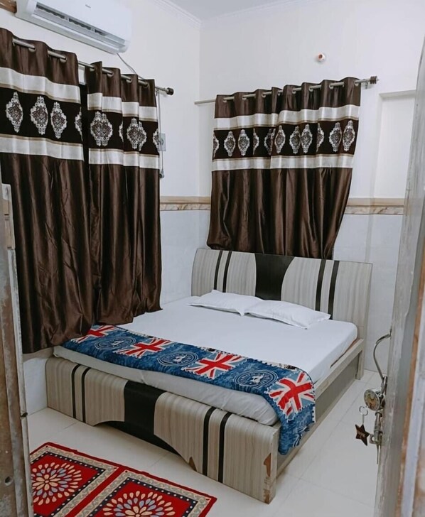 Ein Schlafzimmer mit Bett, Vorhängen, einem Nachttisch und einem gemusterten Teppich.