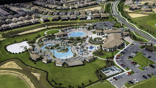 Vue aérienne d’un quartier résidentiel avec un complexe de piscines, des routes et des voitures garées.