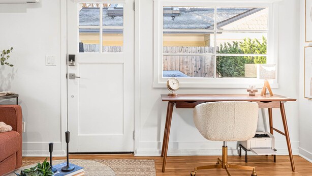 A room with a wooden desk, a chair, a door, and a window with a view of a house and trees. - The Hydeaway at Hyde Park (Boise)