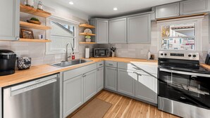 A modern kitchen with grey cabinets, wooden countertops, a dishwasher, a microwave, and a stove. - The Hydeaway at Hyde Park (Boise)