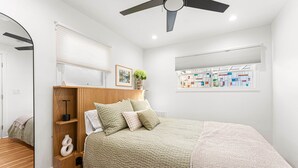 A bedroom with a bed, wooden headboard, bedside tables, a mirror, a ceiling fan, and a window with blinds. - The Hydeaway at Hyde Park (Boise)