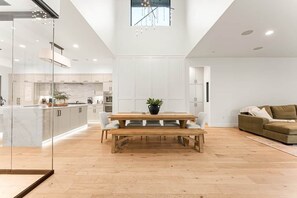 Une cuisine moderne et spacieuse, dotée de meubles blancs, d’une table à manger en bois avec des bancs, et d’une grande fenêtre au-dessus de l’évier.