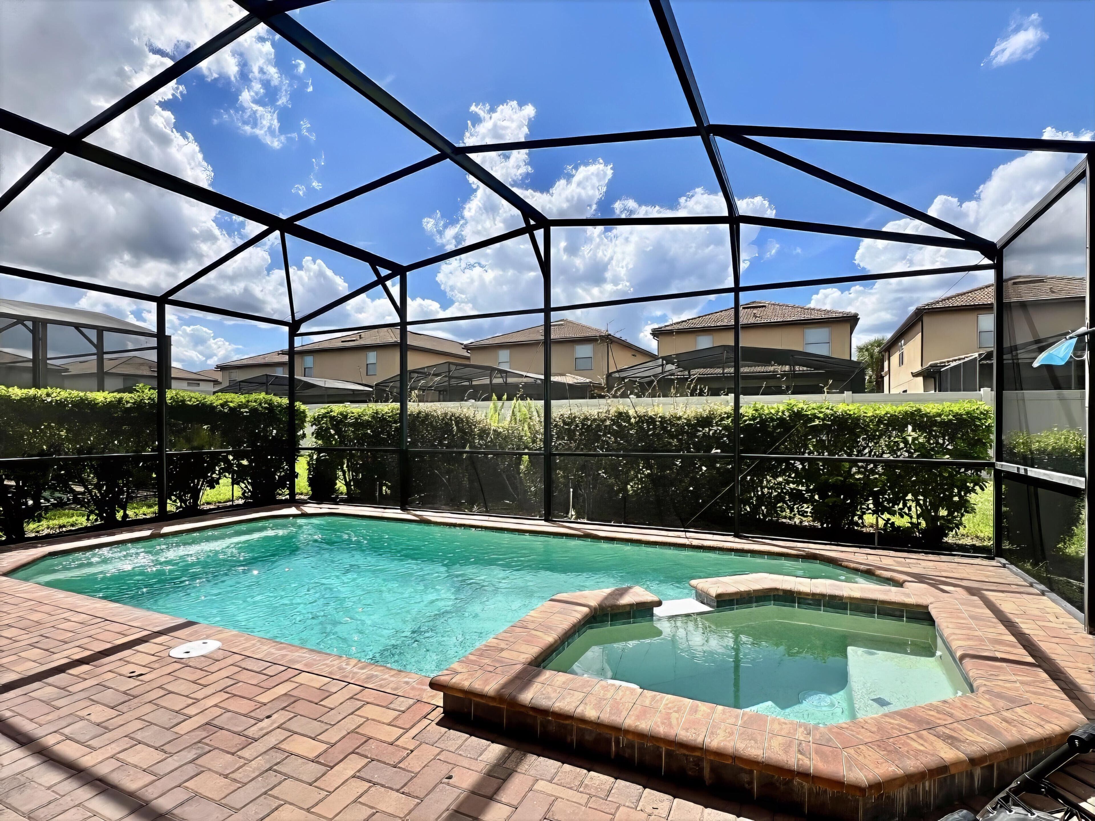 A swimming pool with a hot tub, surrounded by a metal fence, with houses in the background.