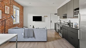 Eine moderne Küche mit grauen Schränken, einem Edelstahl-Kühlschrank und einem flachbildfernseher an der Wand.