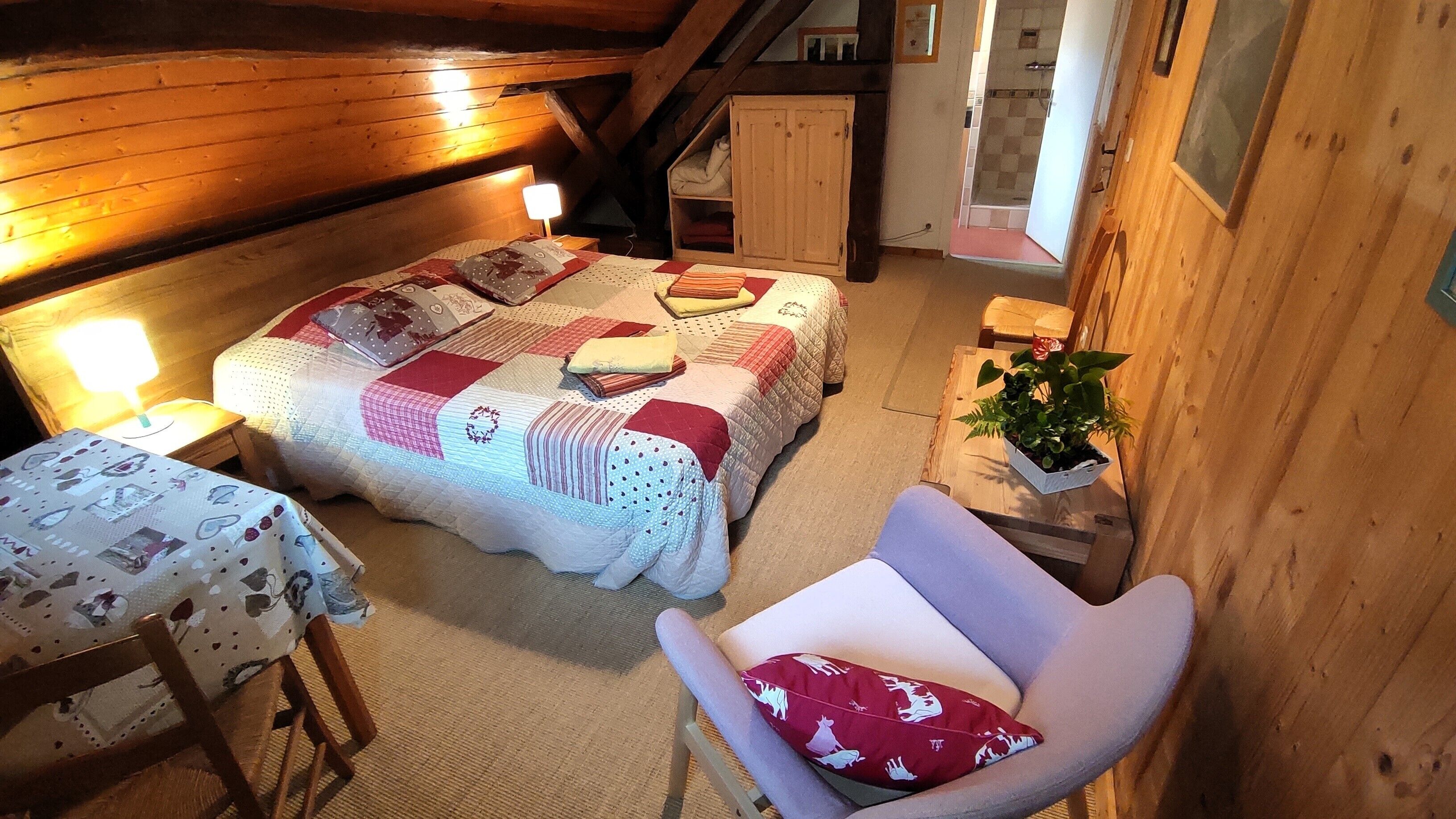 A cozy bedroom with two beds, a small table, a chair, and a wooden cabinet.