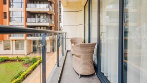 Un balcone con mobili in vimini, ringhiera in vetro e vista su un edificio a più piani con balconi.
