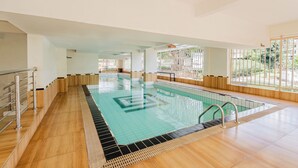 Una piscina interna con pareti in vetro trasparente, pavimento in legno e ringhiere in metallo.