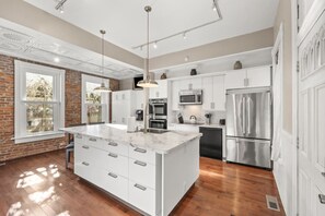 Een moderne keuken met een groot eiland, witte keukenkastjes, roestvrijstalen apparatuur en hanglampen.