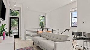 Una sala de estar moderna con un sofá, una mesa de comedor y sillas. Se ve una escalera con barandilla que sube a un nivel superior.