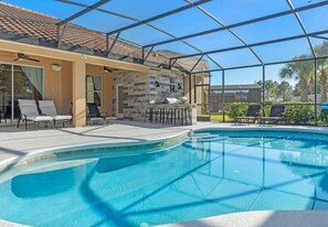 Ein Swimmingpool mit Liegestühlen und einer Grillgegend, umgeben von einer überdachten Terrasse.