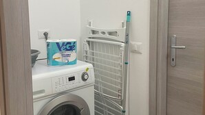 A compact laundry area with a front-loading washing machine, a basket, and a drying rack. - Just minutes from Ogliastra's most beautiful beaches, rooms with en suite facilities (Cardedu)