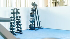 A gym with weightlifting equipment, a blue mat floor, and a white wall with vertical blinds. - Comfy One Bed Room Apartment at Lennox (Accra)