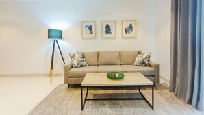 A living room with a sofa, a coffee table, a floor lamp, and three framed artworks on the wall. - Comfy One Bed Room Apartment at Lennox (Accra)