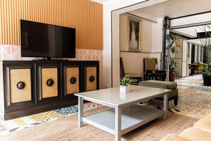 Ein modernes Wohnzimmer mit Flachbildfernseher, einer Couch, einem Couchtisch und einem gemusterten Teppich.