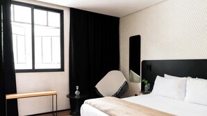 Una habitación de hotel con una cama grande, una silla, una mesita con una lámpara y un banco junto a la ventana.