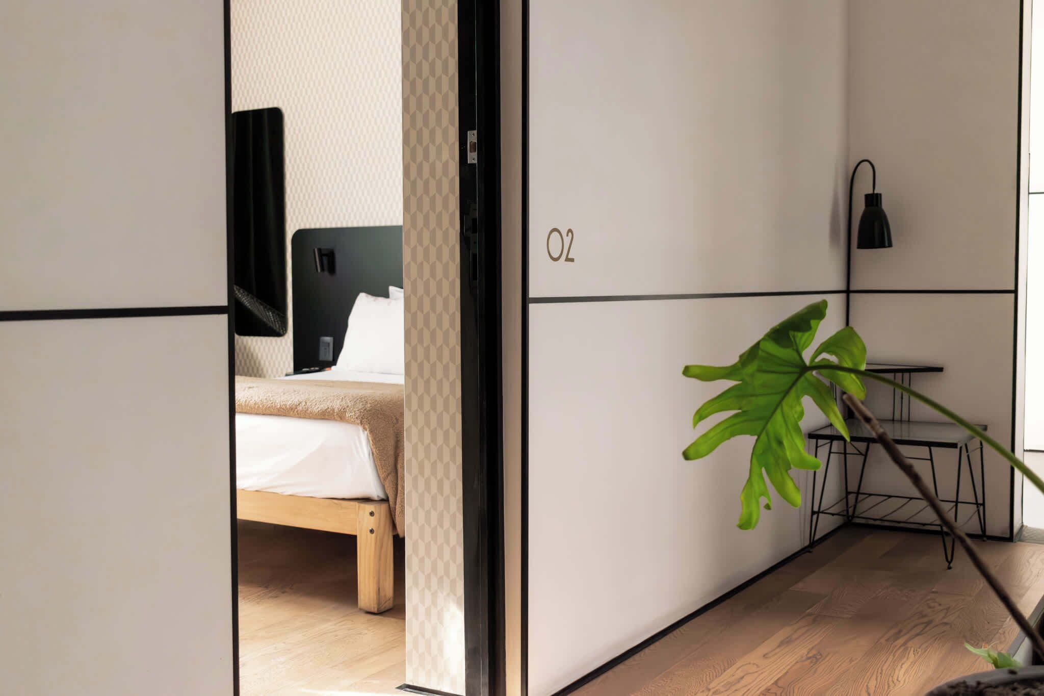 Quarto de hotel moderno com cama, escrivaninha e uma grande planta.