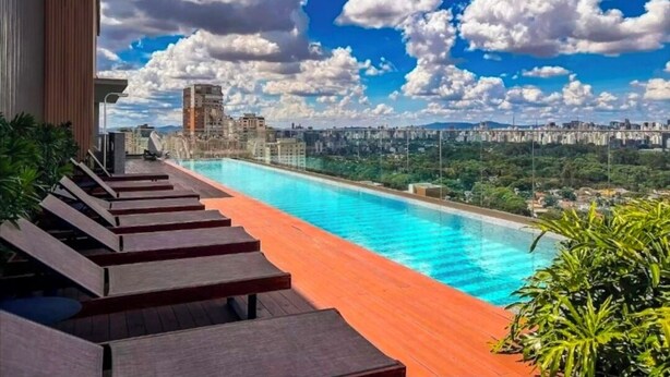 Ein Pool mit Infinity-Kante auf dem Dach, ausgestattet mit Holzliegen, unter blauem Himmel mit Stadtansicht im Hintergrund.